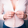 woman's cleavage while buttoning her shirt