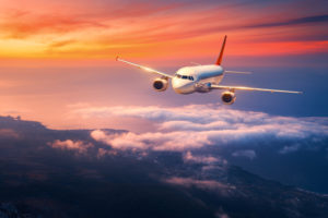 Passenger airplane. Landscape with big white airplane is flying in the sky over the clouds and sea at colorful sunset. Passenger aircraft is landing at dusk. Business trip. Commercial plane. Travel